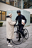 Fahrradkurier nimmt bei der Auslieferung eines Pakets ein Zeichen von einer Kundin entgegen