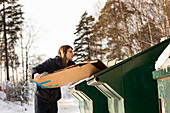 Young man putting cardboard box into recycling bin