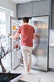 Mann stehend vor offenem Kühlschrank
