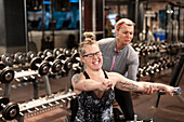 Frau im Rollstuhl trainiert im Fitnessstudio mit Personal Trainer