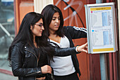 Freundinnen prüfen den Fahrplan an der Bushaltestelle