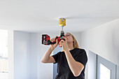 Female electrician drilling in ceiling