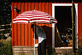 Man unfolding parasol in front of shed