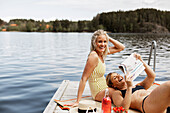 Smiling women in swimsuits reading newspaper at lake