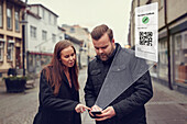 Mann und Frau stehen auf der Straße und überprüfen ihr Telefon mit dem Covid-19-Impfschein