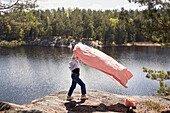 Woman with picnic blanket standing on cliff over lake