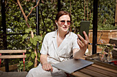Frau sitzt auf der Terrasse und führt einen Videoanruf per Telefon