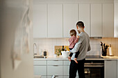 Father carrying toddler girl in kitchen