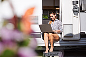 Woman sitting at caravan door and using laptop