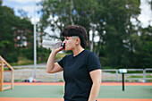 Junge Frau trinkt Wasser im Fitnessstudio im Freien