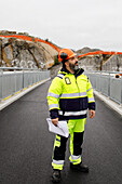 Männlicher Ingenieur in reflektierender Kleidung auf einer Brücke stehend