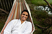 Lächelnder junger Mann im Bademantel entspannt sich in der Hängematte