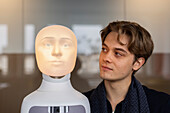 Young man looking at robot voice assistant
