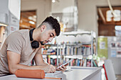 Männlicher Student macht sich in der Bibliothek Notizen