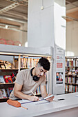Männlicher Student macht sich in der Bibliothek Notizen