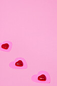 Pink paper hearts and candies on pink background