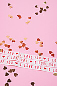 Heart-shaped confetti and love message on pink background