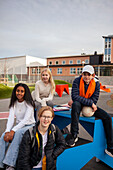 Portrait of teenage friends sitting in front of school