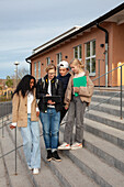 Teenage friends standing in front of school and using laptop