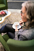 Senior woman sitting in armchair and drinking coffee