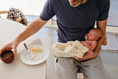 Father holding newborn baby and eating breakfast