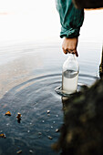 Hand einer Frau, die eine Glasflasche mit Wasser füllt