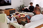 Familie entspannt sich im Wohnzimmer und benutzt Telefon und Tablet