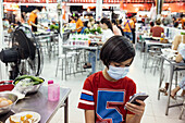 Boy in face mask using phone in food court