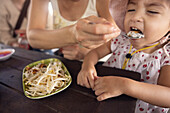 Mutter füttert Tochter mit asiatischem Essen