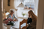 Grandmother and adult granddaughter sitting at table and having tea