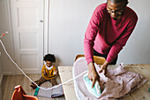 Vater bügelt Wäsche, während Tochter auf dem Boden spielt