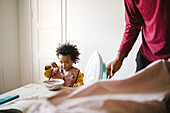 Girl eating from bowl while father ironing clothes