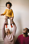 Mother lifting smiling daughter at home