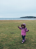 Mädchen in rosa Winterkleidung geht an der Küste spazieren