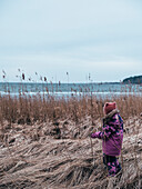 Girl in pink winter clothes walking among reeds on coast