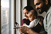 Vater und Mutter mit Baby schauen durch das Fenster