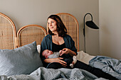 Mother relaxing in bed with sleeping newborn baby