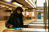 Frau, die mit ihrem Smartphone eine Fahrkarte für die U-Bahn bezahlt