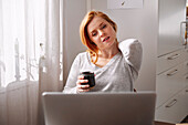 Woman holding her neck while using laptop