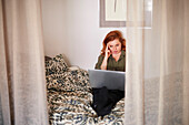 Lächelnde Frau mit Laptop auf dem Bett