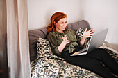 Smiling woman using laptop on bed