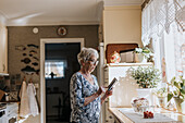 Ältere Frau telefoniert mit Handy in der Küche
