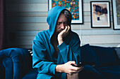 Sad man with smartphone sitting on sofa