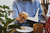 Woman reading book and eating cinnamon bun