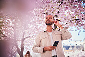 Junger Mann, der unter einer Kirschblüte steht und telefoniert