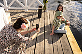 Mutter fotografiert Kinder auf dem Bootssteg sitzend
