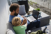 Father sitting with son on deck and working on laptop