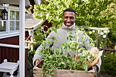Smiling man holding crate with tomato plants
