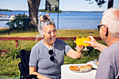 Senior couple having meal and rising toast at camp site