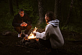 Couple sitting by campfire in forest